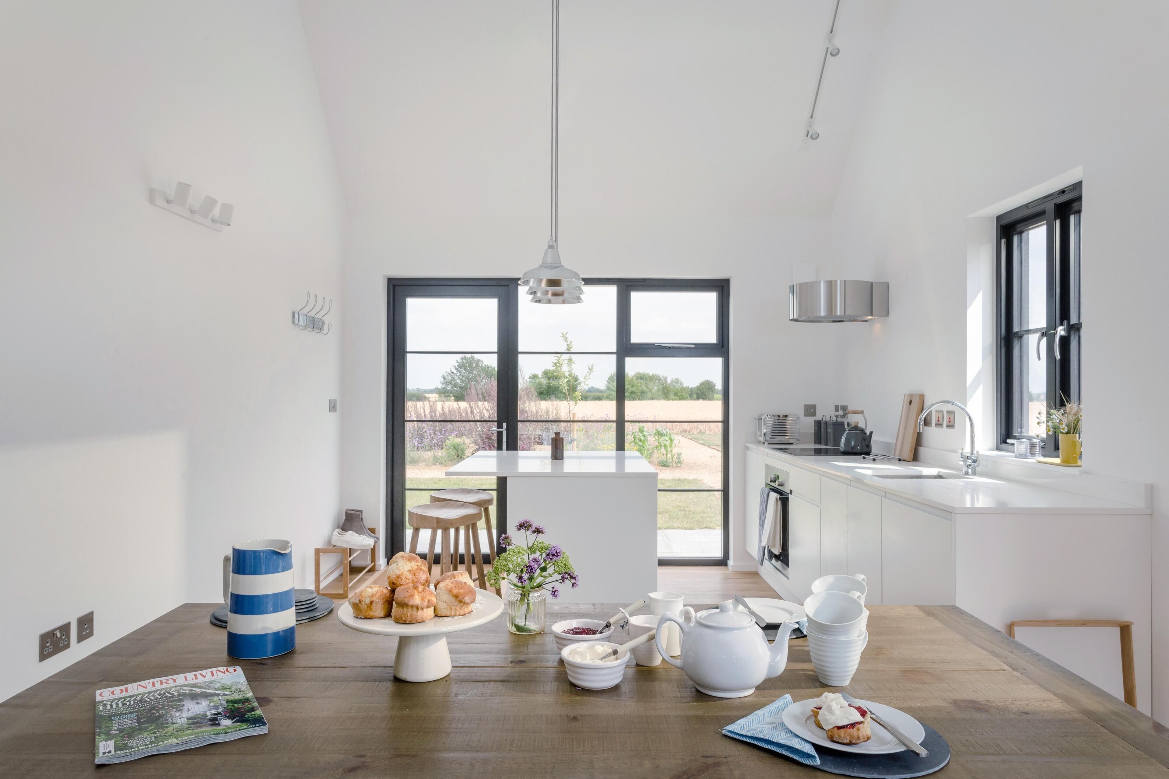 A modern kitchen with a dining area, large windows, and a view of the outdoors.
