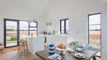 A modern kitchen with a large island, wooden stools, and a view of the countryside through large windows.