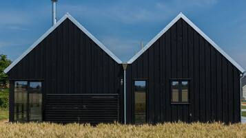 Un bâtiment en bois noir, doté d’un toit en pente, d’une cheminée et d’une porte de garage.