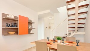 A dining area with a wooden table, orange chairs, and a staircase with wooden railings.