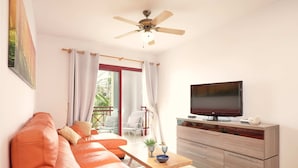A living room with a leather sofa, a TV on a wooden cabinet, and a ceiling fan.