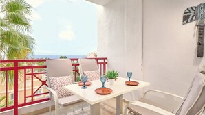 A balcony with a table set for two, chairs, and a view of the ocean.