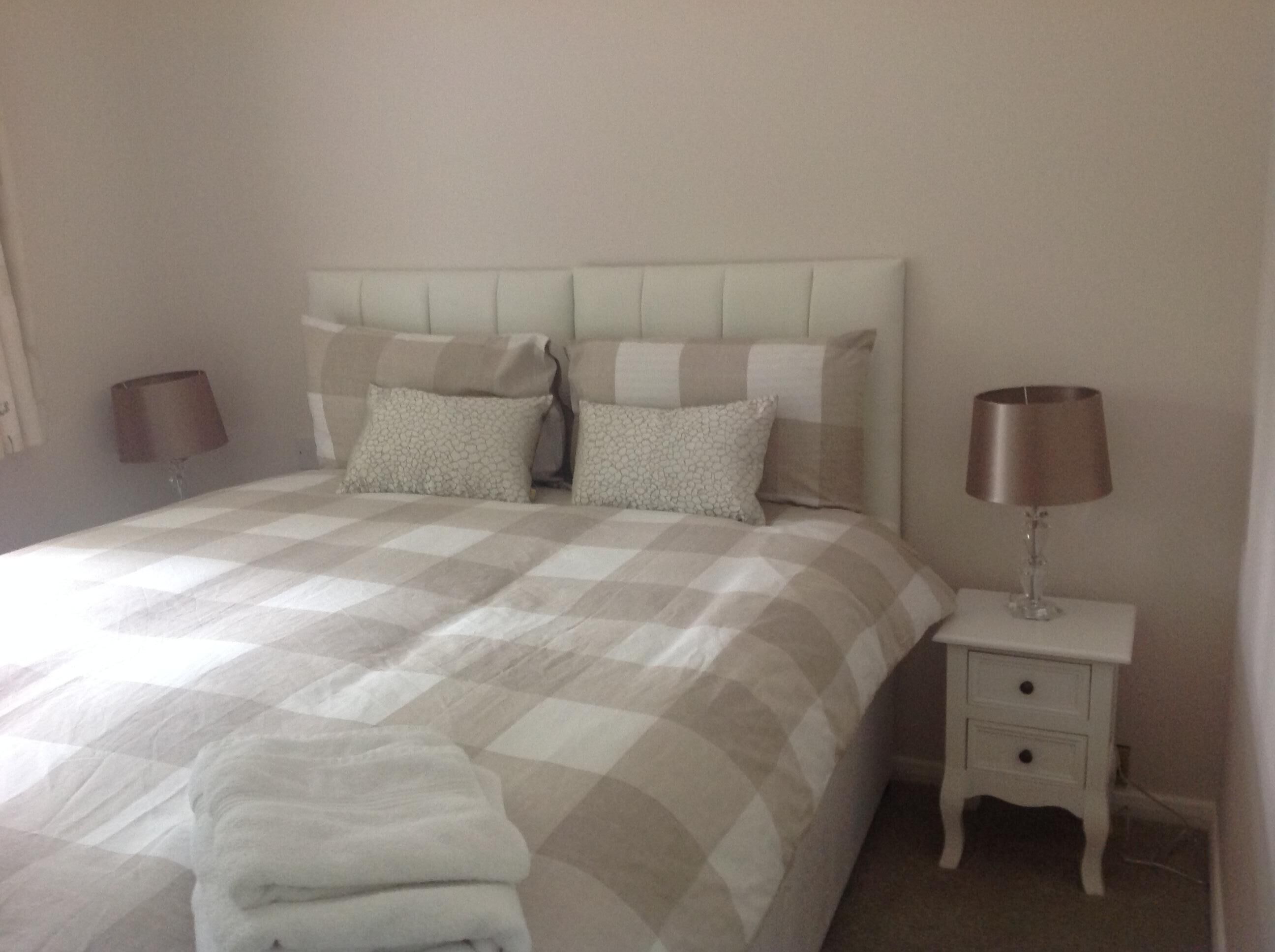 A neatly made bed with a checkered bedspread, two pillows, and a bedside lamp on a white nightstand.