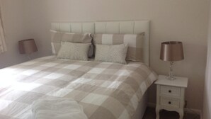Een net opgemaakt bed met een geruit sprei, twee kussens en een bedlampje op een witte nachtkastje.