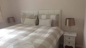 A neatly made bed with a checkered bedspread, two pillows, and a bedside lamp on a white nightstand.
