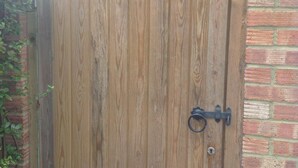 Een houten hek met een metalen grendel, voor een bakstenen muur.
