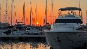 Uma marina com vários barcos atracados, céu claro e o sol se pondo ao fundo.
