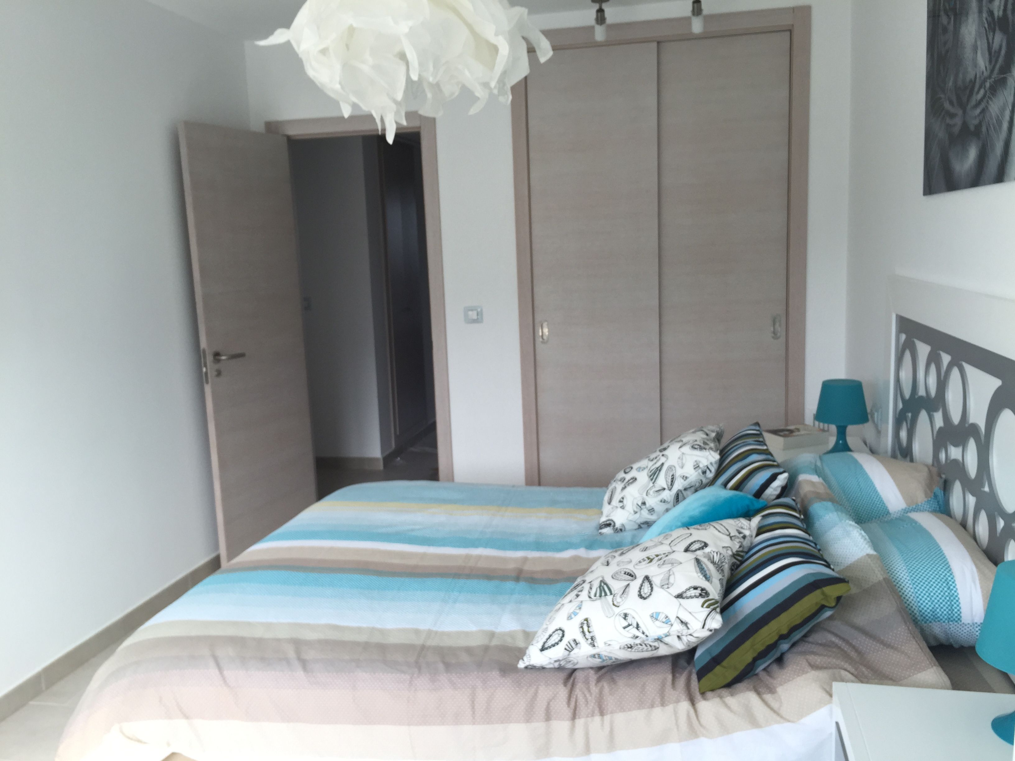 A bedroom with a bed, pillows, a nightstand, a lamp, and a wardrobe.