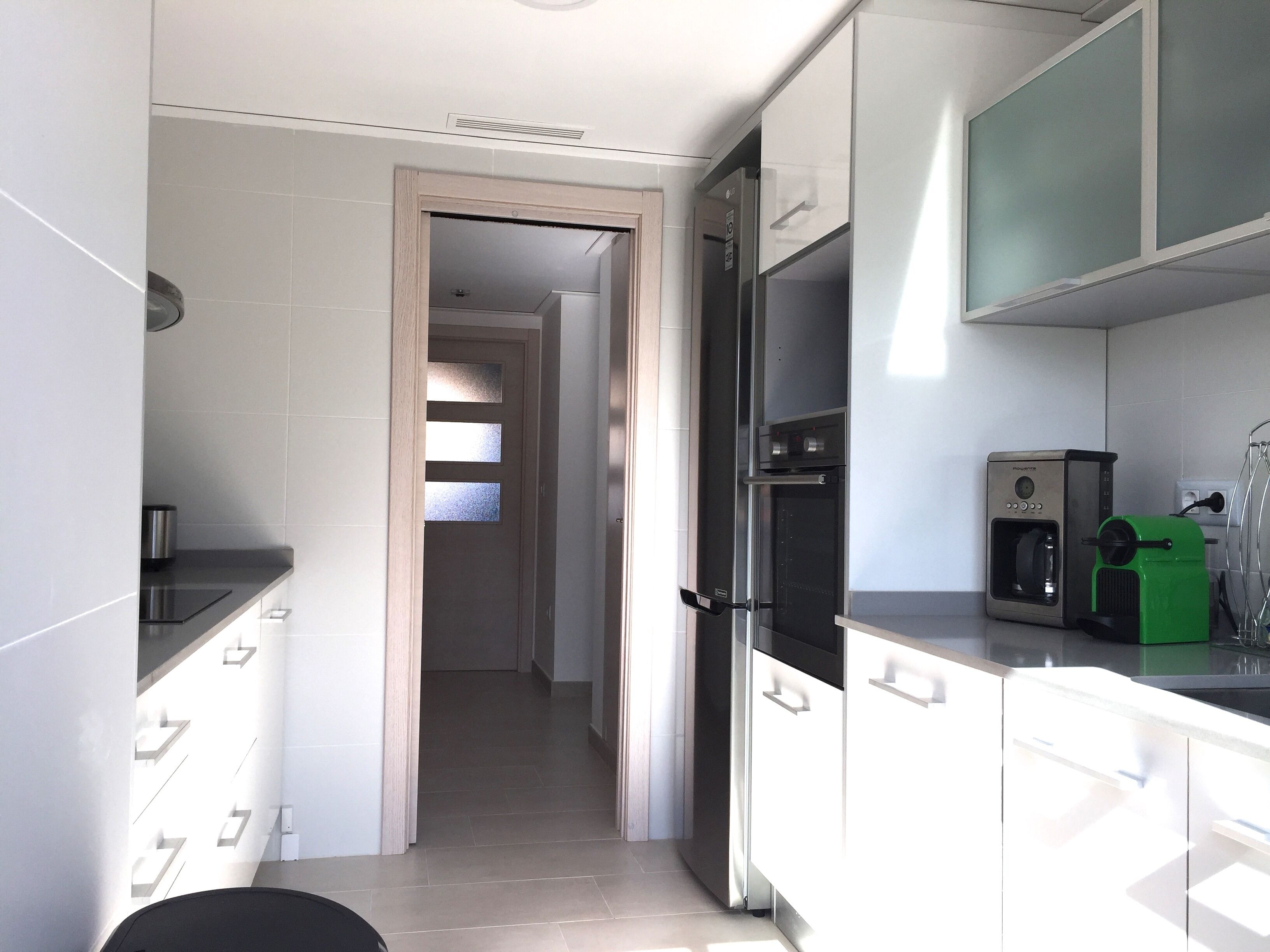 Een moderne keuken met witte kasten, een inbouwoven en een koffieapparaat.