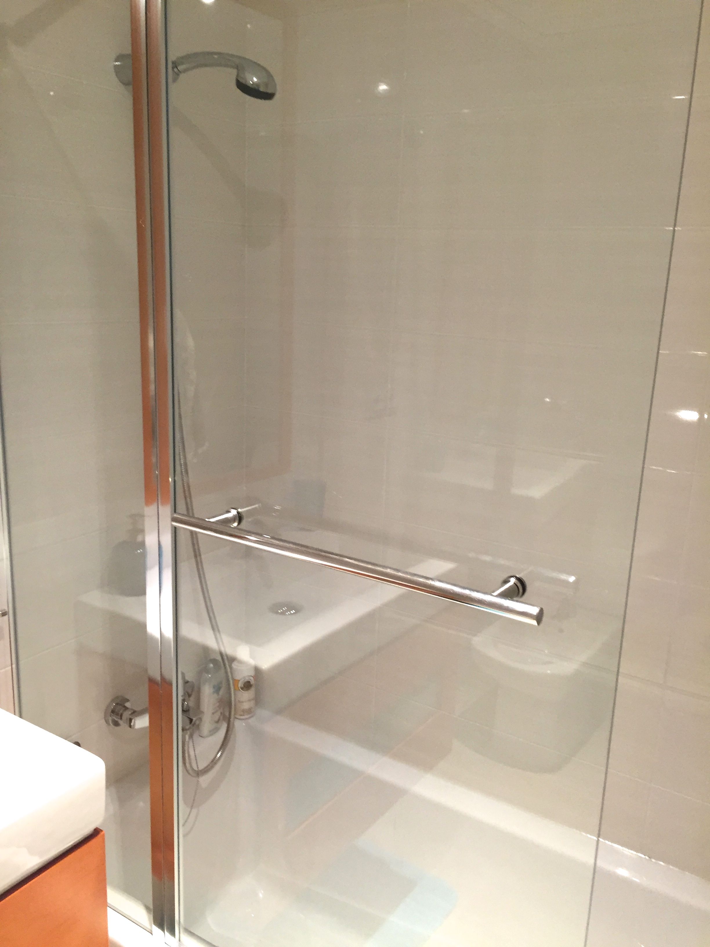 A glass-enclosed shower with a handheld showerhead and a handheld shower bar.