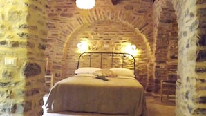 A stone-walled bedroom with a bed, a chandelier, and a staircase leading to the bed. - XVII SEC.  WINE CELLAR, FULLY RENOVATED, WITH SHARED TERRACE AND POOL (Badalucco)