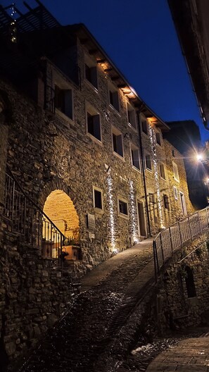 Un bâtiment en pierre avec un escalier menant à une porte, le tout éclairé par une lumière chaleureuse.
