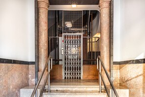 A marble staircase with metal railings leading to a gated elevator area.