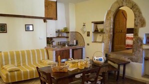Ein gemütliches Wohnzimmer mit einem gestreiften Sofa, einem Holzespeisetisch mit Stühlen und einem steinernen Bogen, der in ein Schlafzimmer führt.