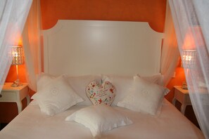 Ein Bett mit weißer Bettwäsche und einem herzförmigen Kopfkissen mit Blumenstickerei.