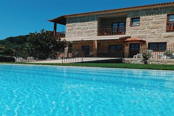 Ein zweistöckiges Steinhaus mit Schwimmbecken davor.