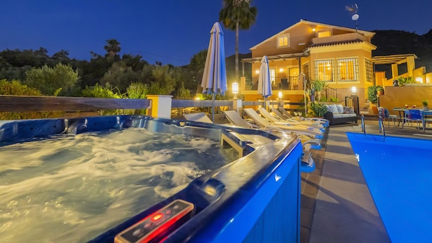 A hot tub area with lounge chairs and umbrellas, a pool, and a building with a balcony in the background. - Cubo's La Casa Grande / Jacuzzi / pool / air conditioning / garden (Cártama)