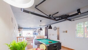 A pool table with a drink, a bowl of chips, and a potted plant in a room with a kitchen area, a clock, and a window. - Cubo's La Casa Grande / Jacuzzi / pool / air conditioning / garden (Cártama)