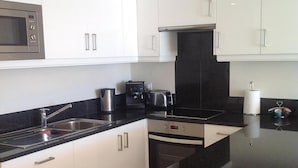 A modern kitchen with white cabinets, a black countertop, stainless steel appliances, and a built-in oven. - Luxury 3 Bedroomed Apartment- Stunning Views, Direct Marina Access & Shared Pool (Vilamoura)