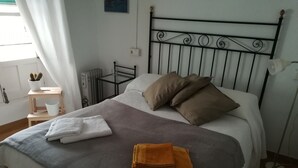 En snyggt bäddad säng med en grå och brun filt, två kuddar och hopvikta handdukar.
