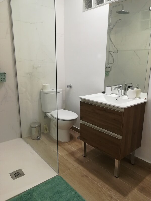 A modern bathroom with a glass shower enclosure, a toilet, a sink with a mirror, and wooden cabinetry.