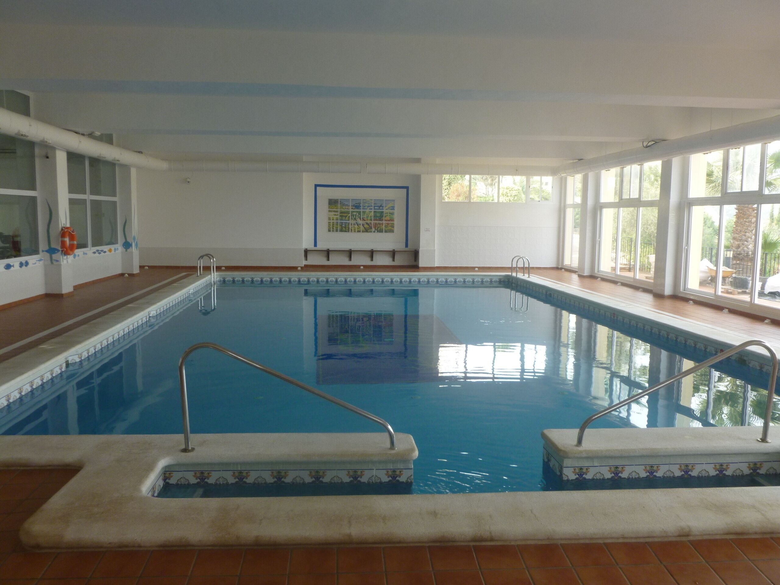 An indoor swimming pool with clear blue water, tiled edges, and a lifebuoy on the left.