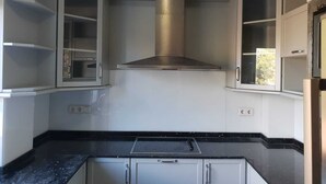 Una cocina compacta con armarios blancos, una campana extractora de acero inoxidable y una encimera negra.