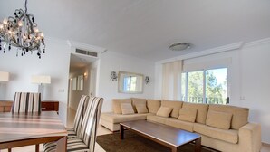 Una sala de estar con sofá, mesa de centro, sillas a rayas, una araña y una mesa de comedor.
