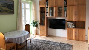 A living room with a wooden cabinet, a television, a dining table with chairs, and a patterned rug. - Modern apartment in Dresden (Dresden)
