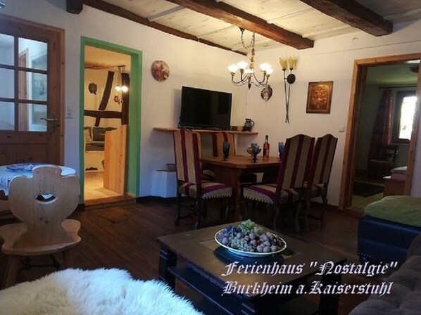 Ein gemütliches Wohnzimmer mit Essbereich, Holzmöbeln, einer Chandelüster und einem Fernseher.