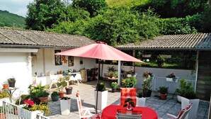 An outdoor patio area with a table and chairs under a red umbrella, surrounded by potted plants and a white fence. - Mediterranean flair above the rooftops of Cochem's old town (Cochem)