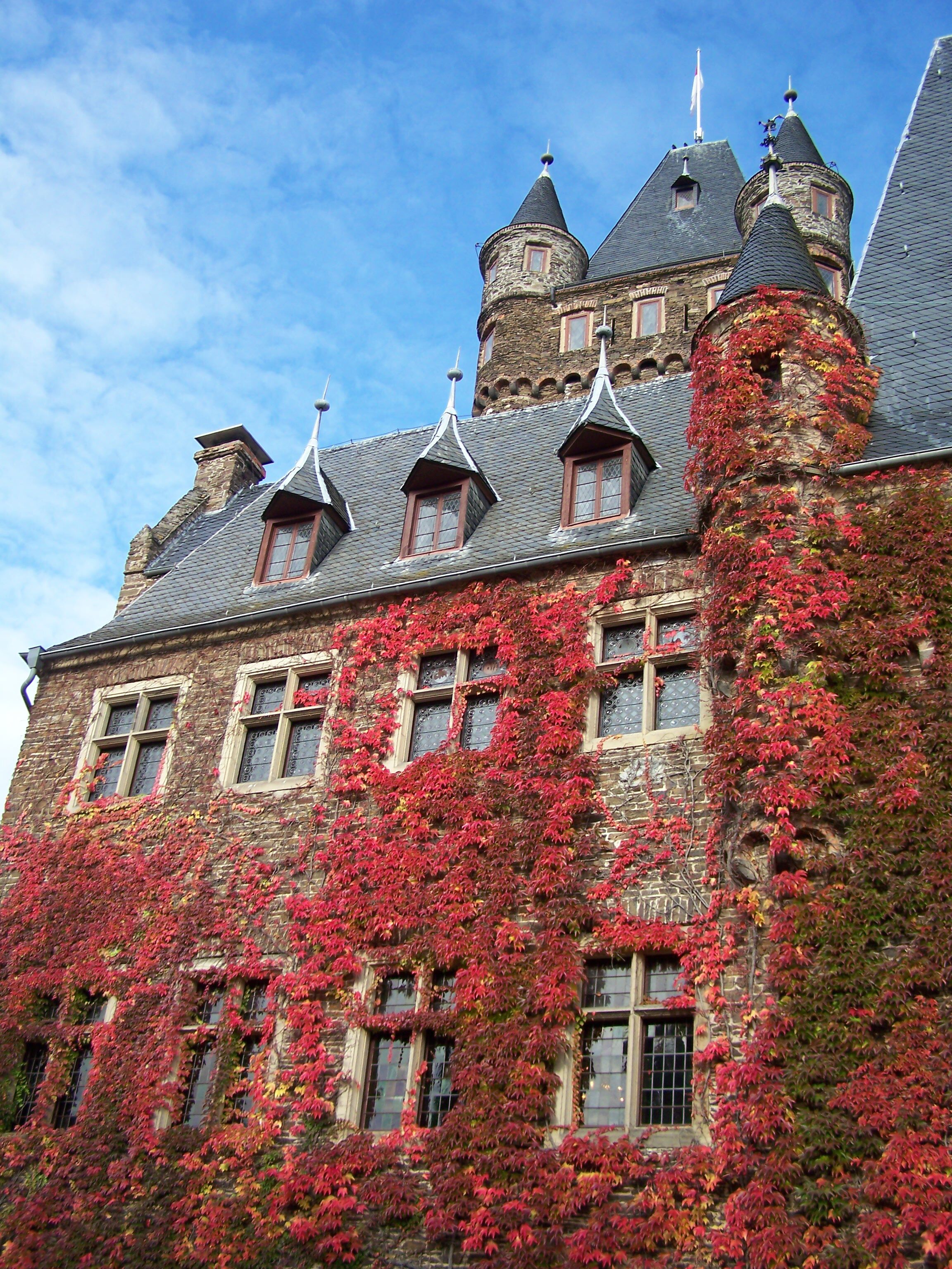 A historic building with a stone facade, multiple windows, and a tower with a conical roof.