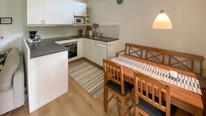 A compact kitchen with white cabinets, a microwave, and a sink. There's a wooden dining table with chairs and a bench. A hanging light fixture is visible. - Awesome home in Löttorp with kitchen (Löttorp)