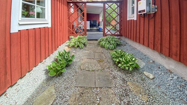 A red building with a gravel pathway leading to a covered entrance. - Awesome home in Löttorp with kitchen (Löttorp)