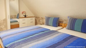 A bedroom with two beds, a dresser, a mirror, and a potted plant.