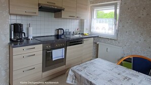 A kitchen with wooden cabinets, a coffee maker, a kettle, and a window with a view of greenery.