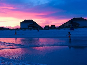 A beach scene with buildings and a person walking on the sand.