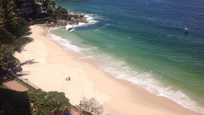 Ein Strand mit klarem Wasser, sandigem Ufer und einem Gebäude mit vielen Fenstern.