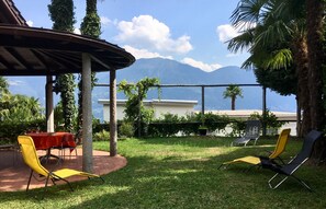 An outdoor seating area with a table and chairs, surrounded by greenery and palm trees, with a mountain view in the background.