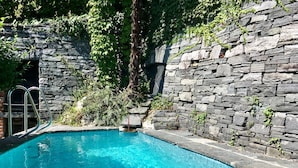 Una piscina con muros de piedra y una escalera metálica.