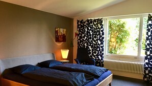 Un dormitorio con cama, una silla, una lámpara, un radiador y una ventana con cortinas.
