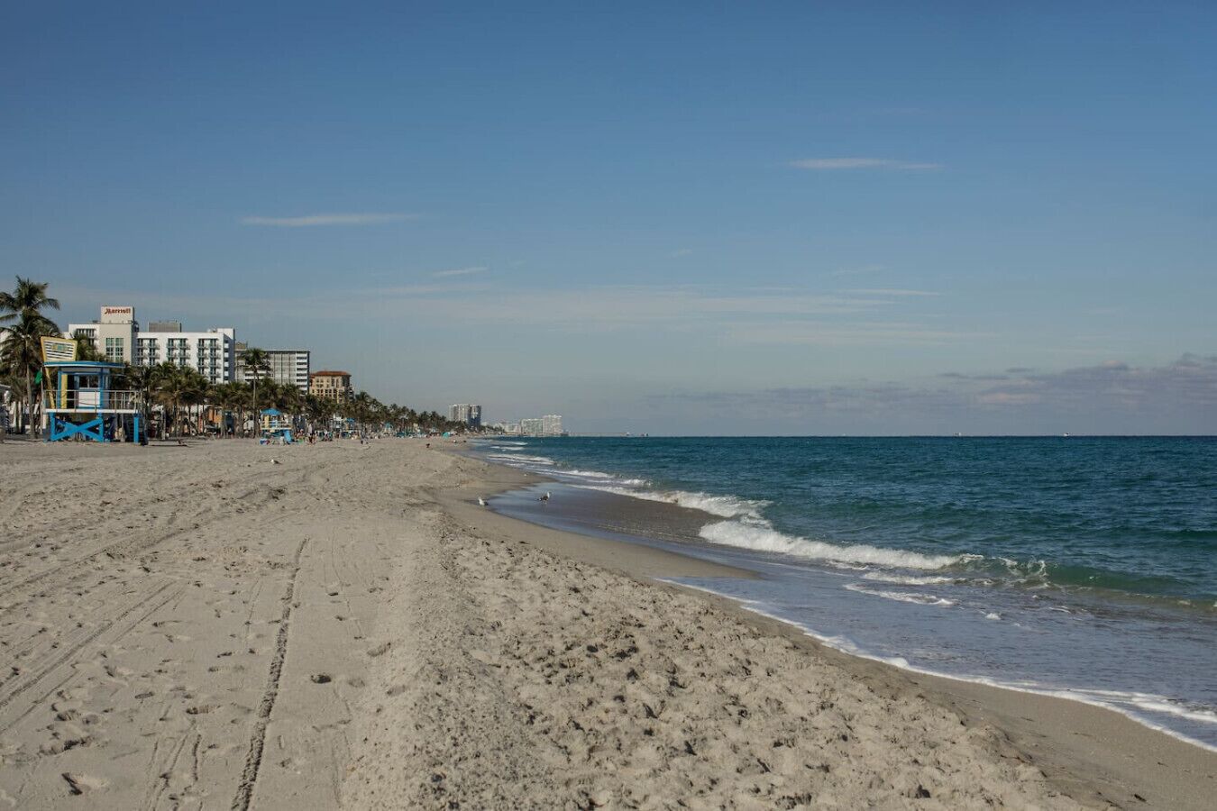 A beach with a lifeguard tower, palm trees, and buildings in the background.