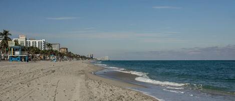 A beach with a lifeguard tower, palm trees, and buildings in the background.