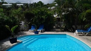 Una piscina azul clara con sillas de descanso y plantas en macetas a su alrededor.