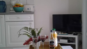 Cocina moderna con armarios blancos, una cafetera, un cuenco de fruta y un televisor sobre un mueble.
