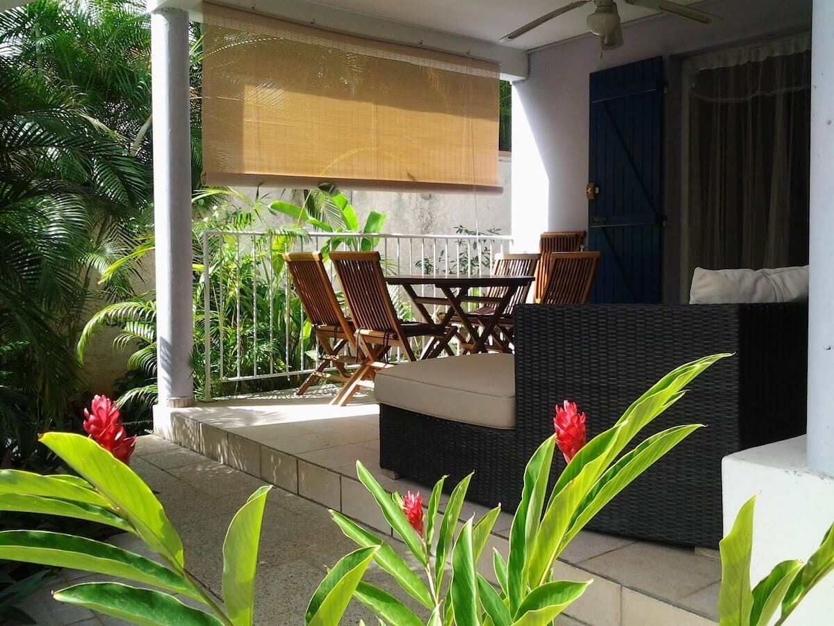Un patio al aire libre con mobiliario de mimbre, un área de estar techada y plantas tropicales.