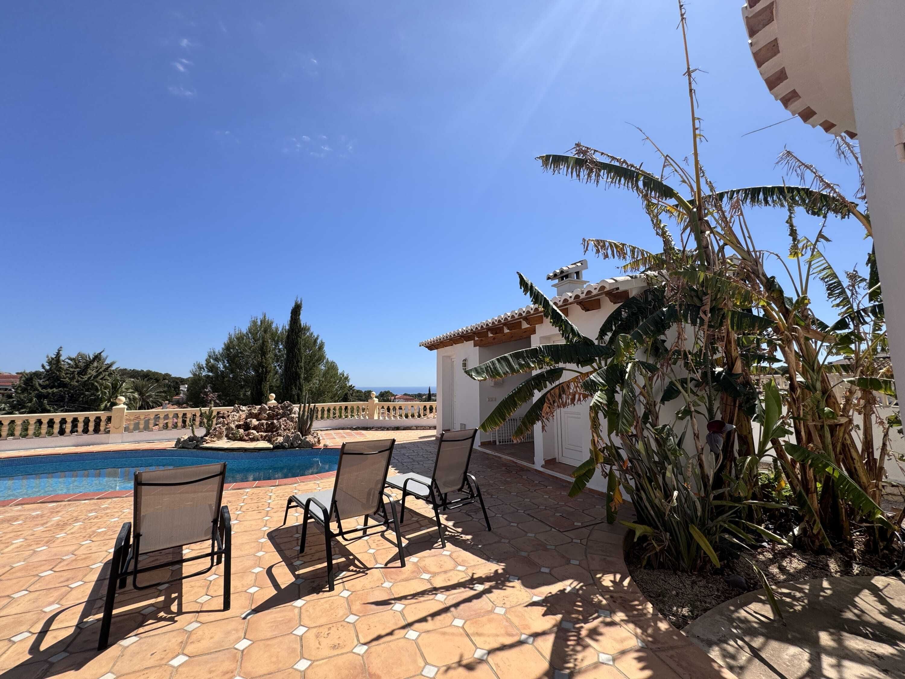 A poolside area with lounge chairs, a tiled patio, and a view of the sea.