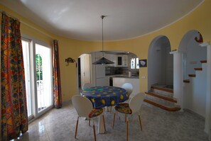 A dining area with a round table, chairs, and a kitchen in the background. - Beatuiful villa with private pool and air-condition (Moraira)
