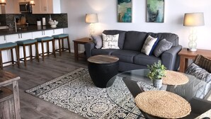 Un salon moderne avec un canapé gris, une table basse et un coin cuisine équipé de tabourets de bar.