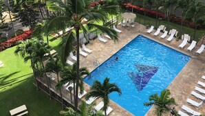 Une piscine entourée de palmiers et de chaises longues, avec en arrière-plan une vue sur un quartier résidentiel.